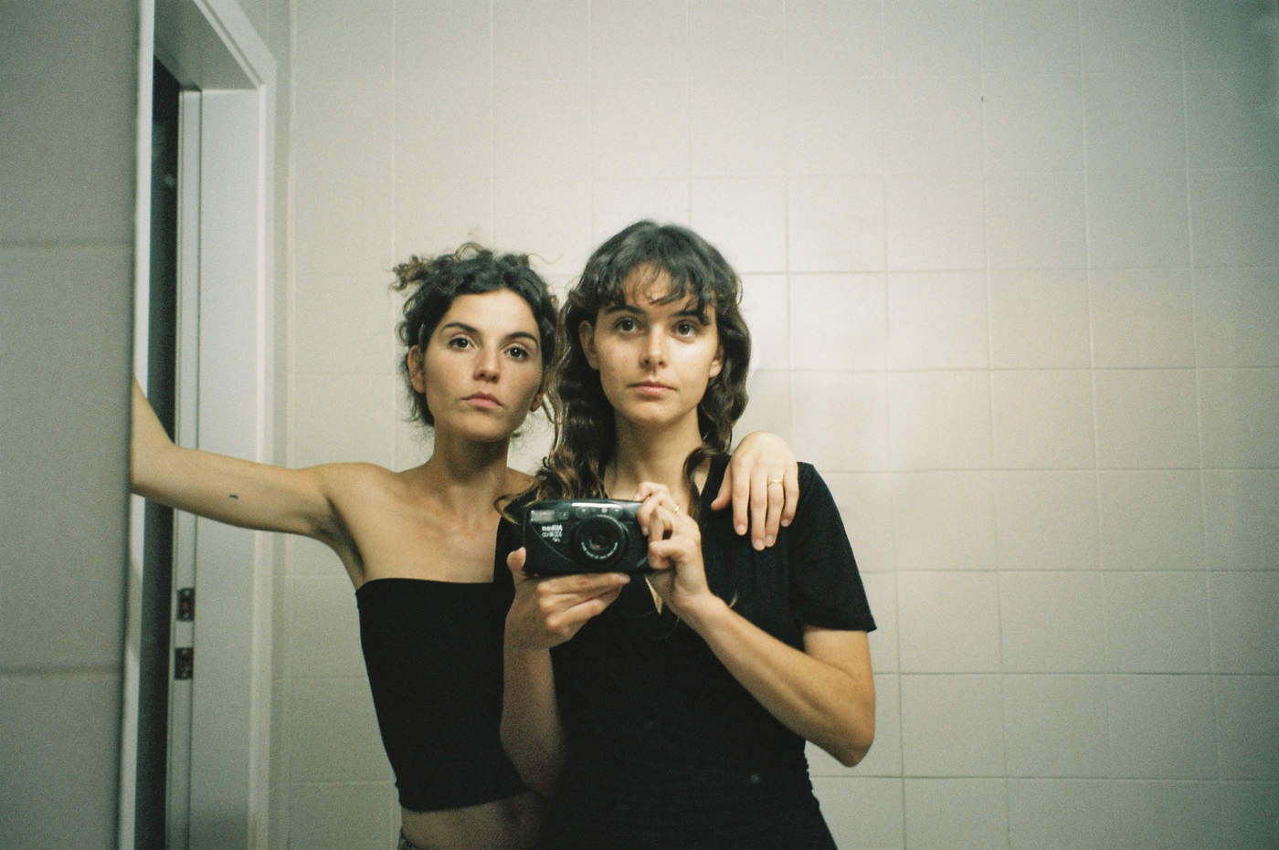 Dos mujeres ante el espejo sosteniendo una cámara de fotos