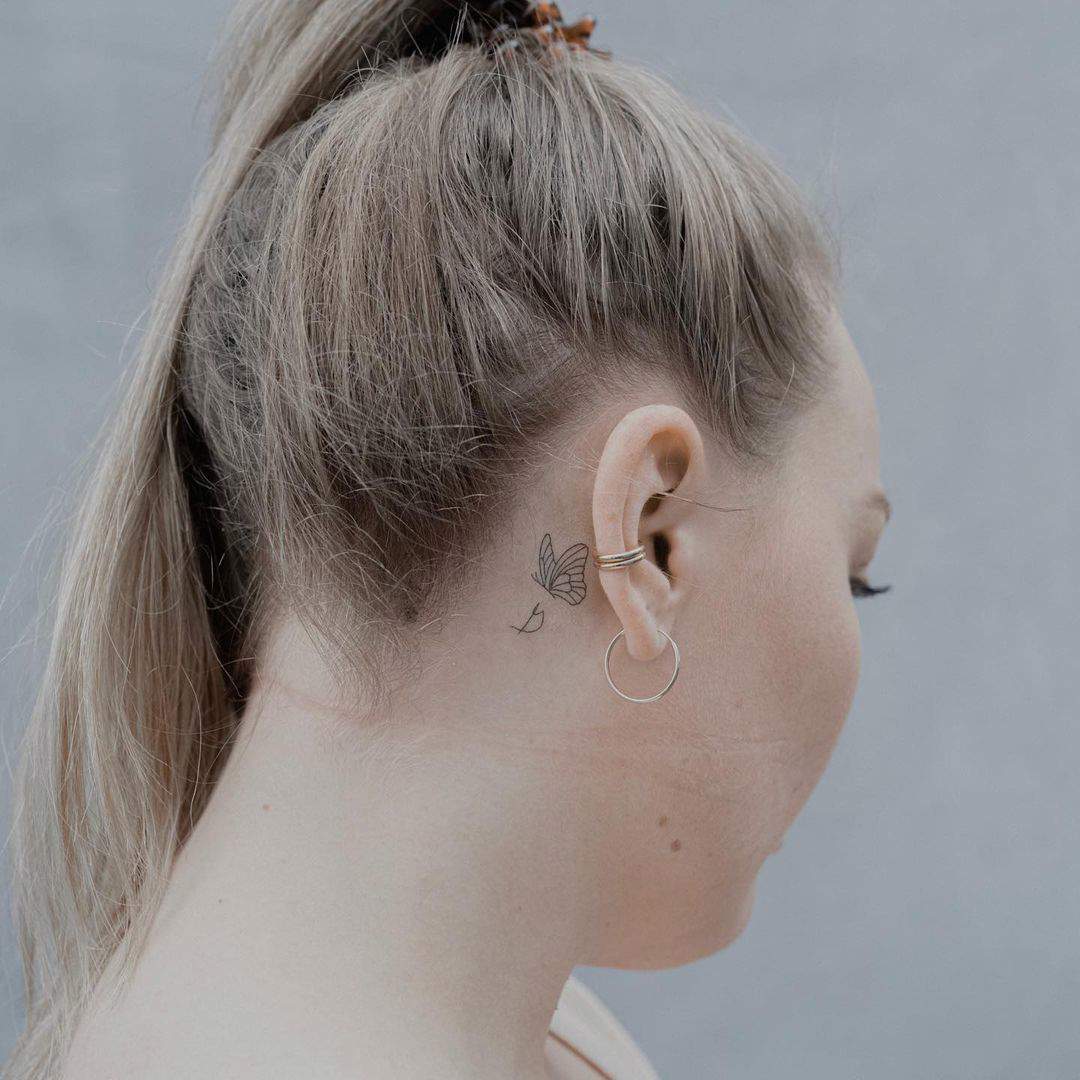 Una mariposa y una inicial tatuadas tras la oreja