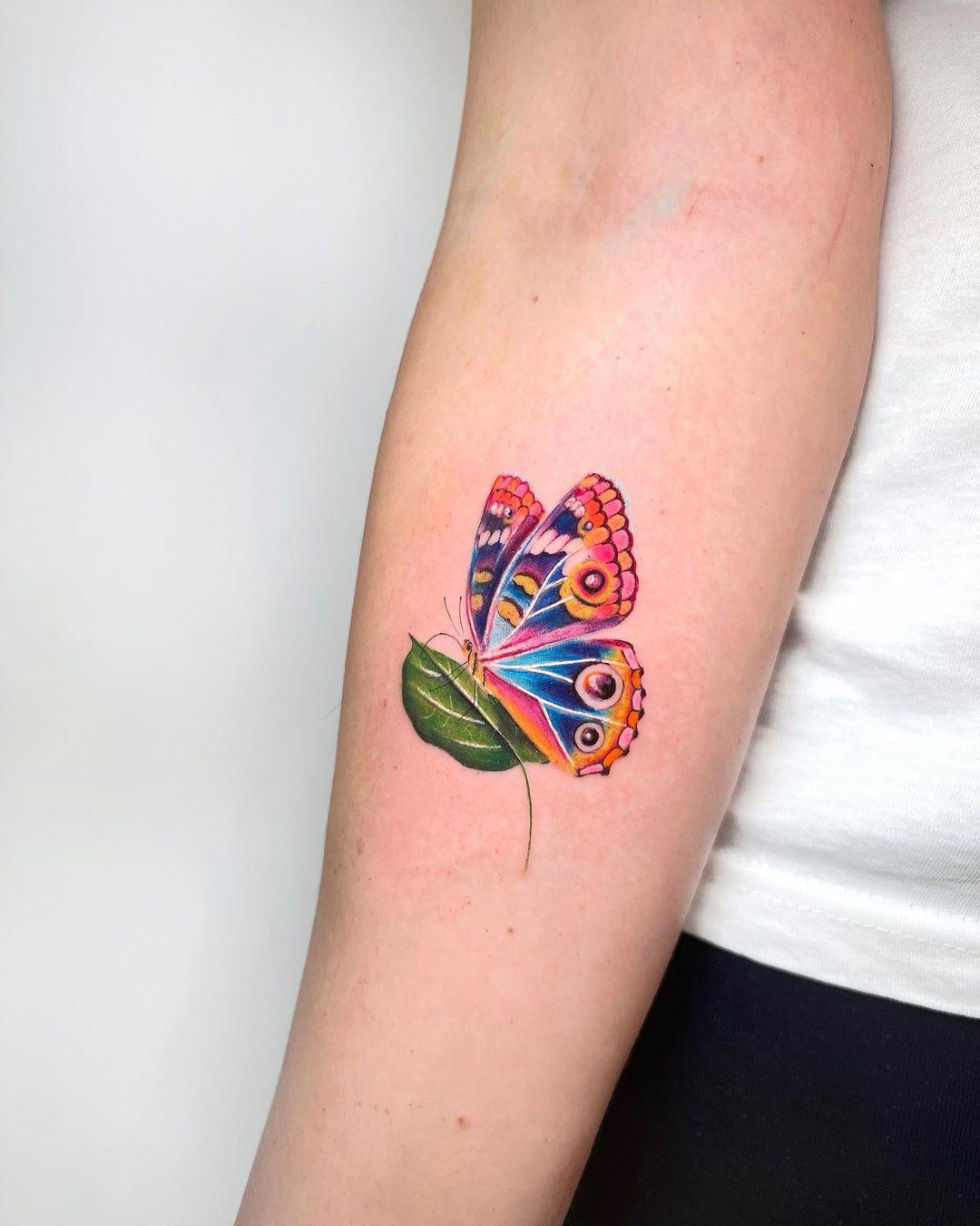 Tattoo en color de una mariposa posada en una hoja