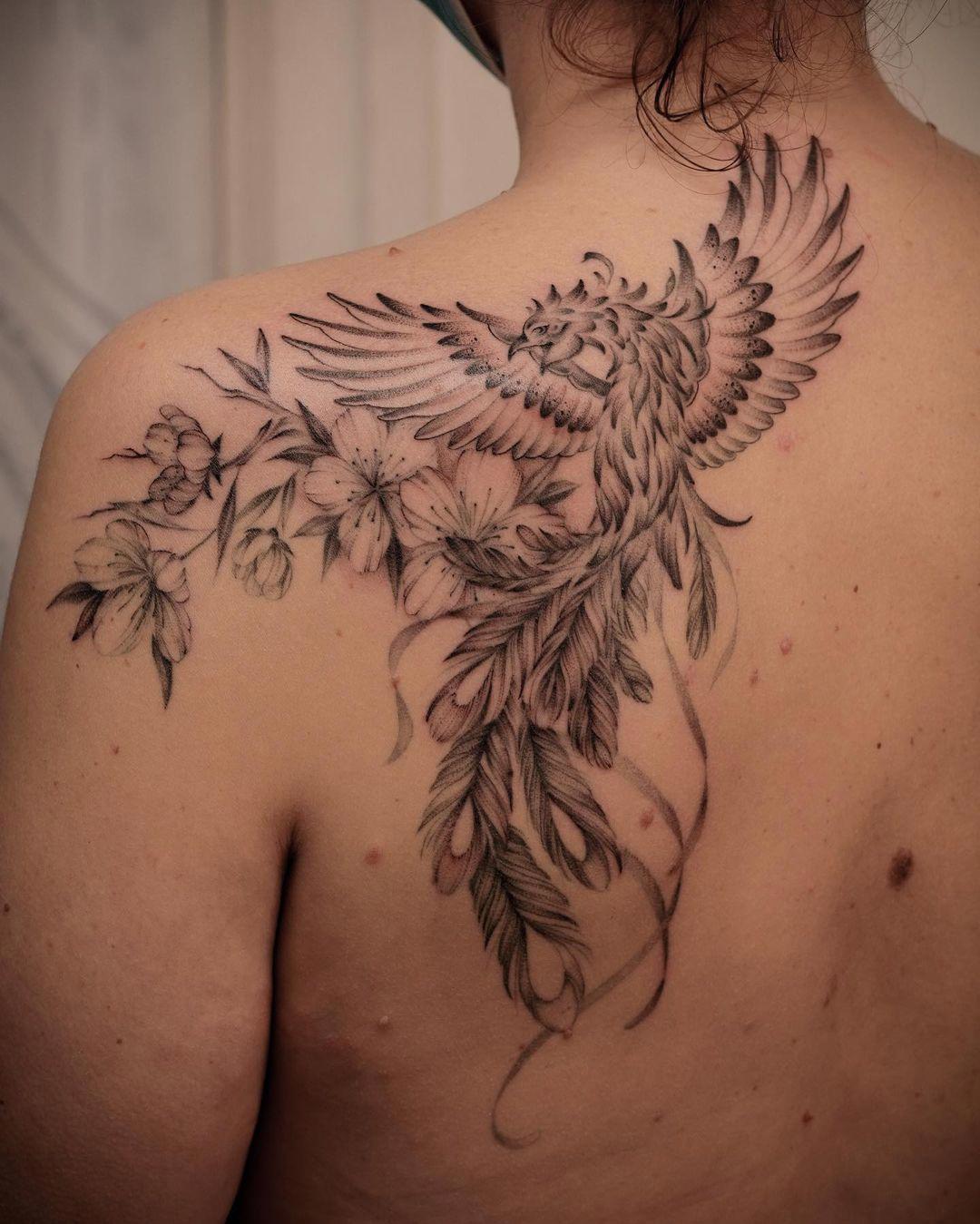 Tattoo en la espalda con un fénix sobre flores