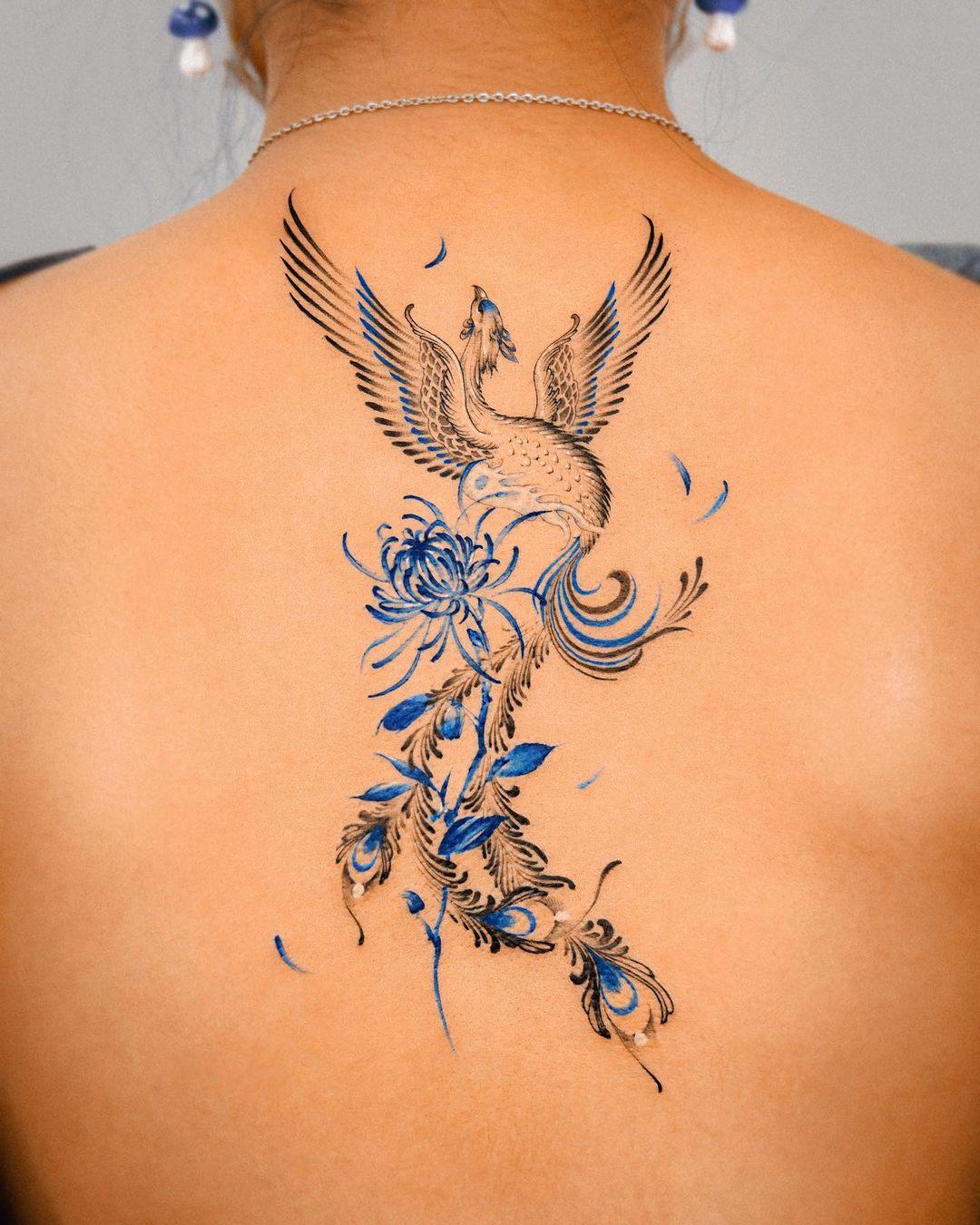 Tattoo en la espalda de ave fénix en azul, blanco y negro