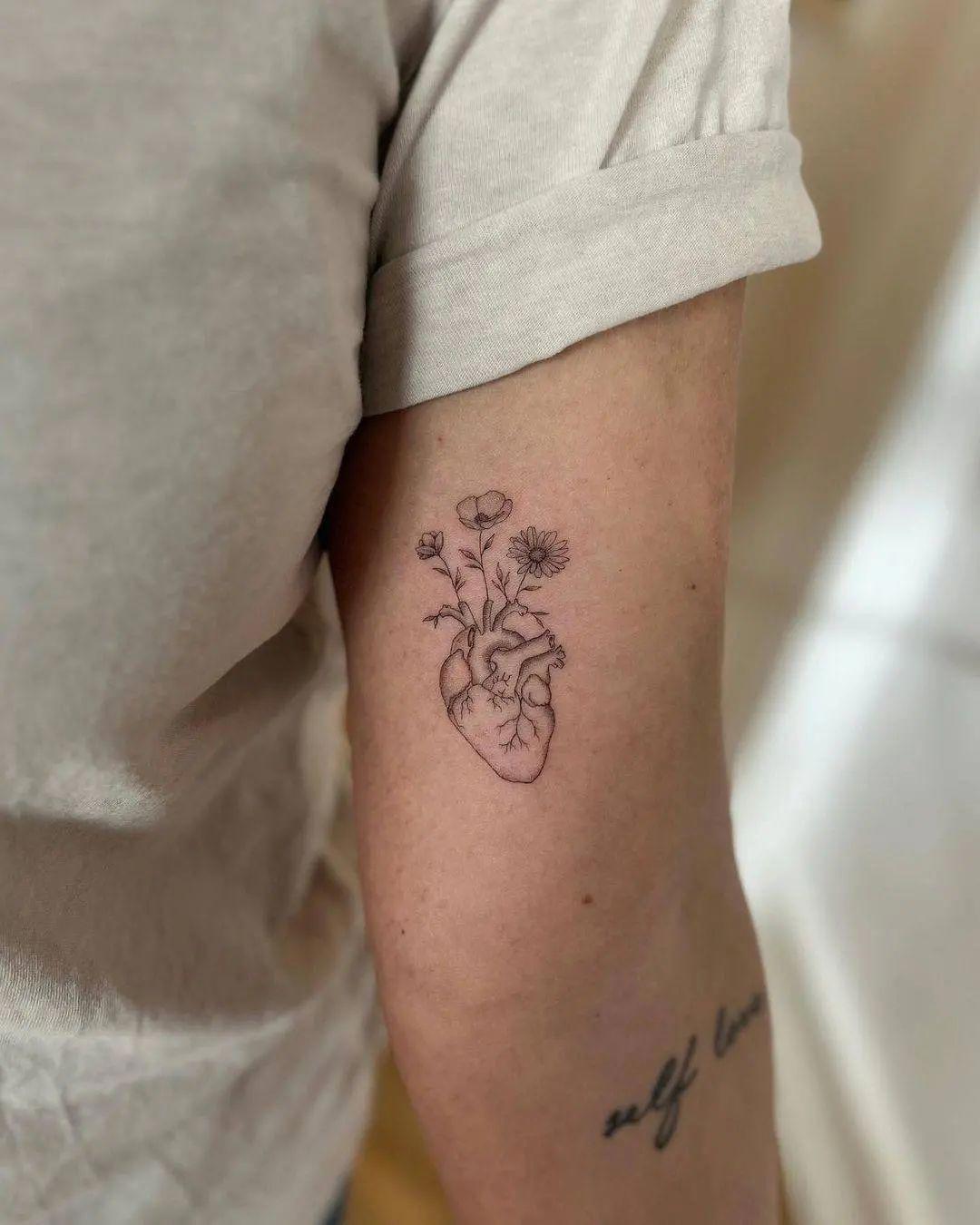 Tatu de corazón con flores en el brazo