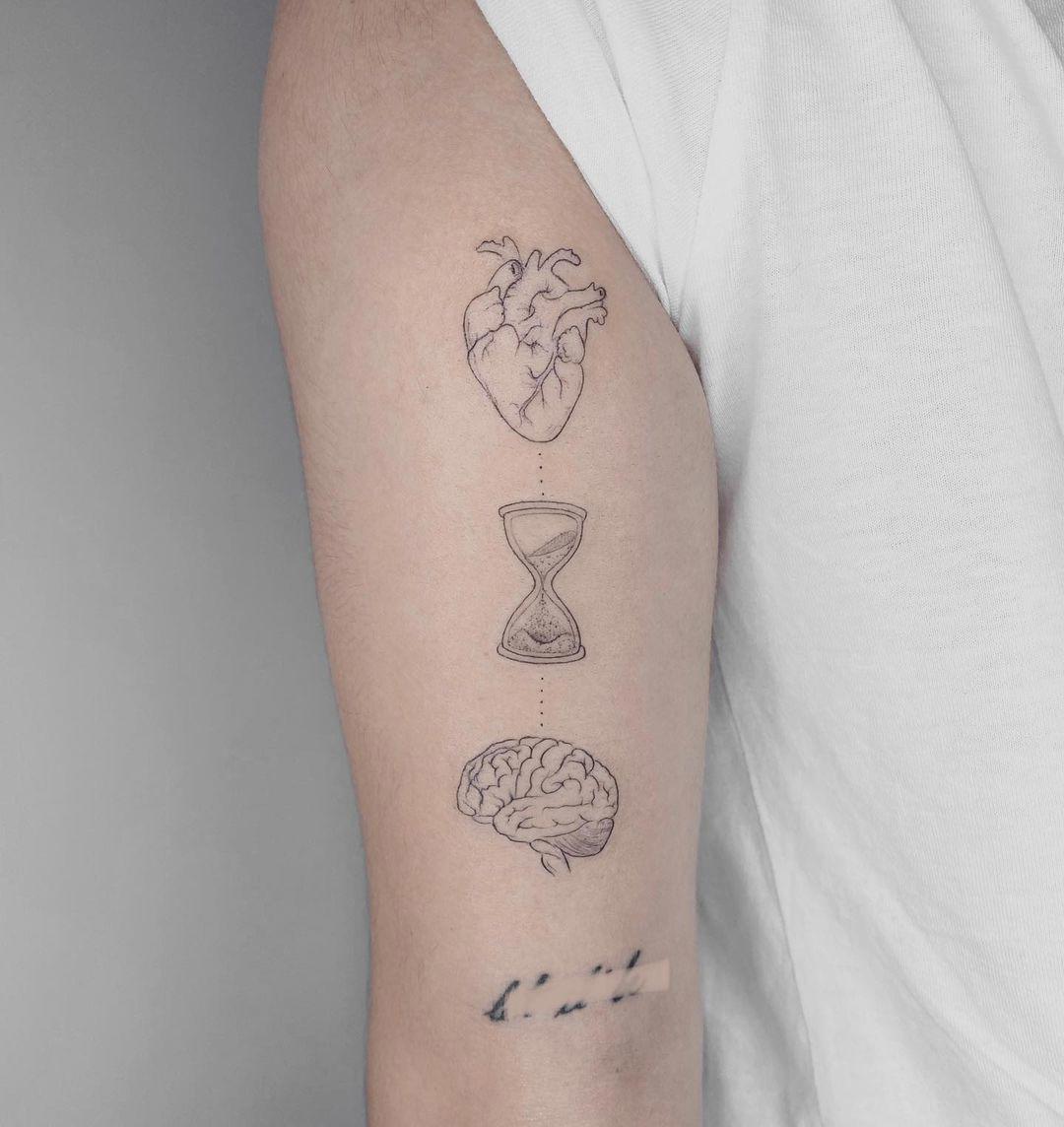 Tatuaje en el brazo de corazón, reloj y cerebro