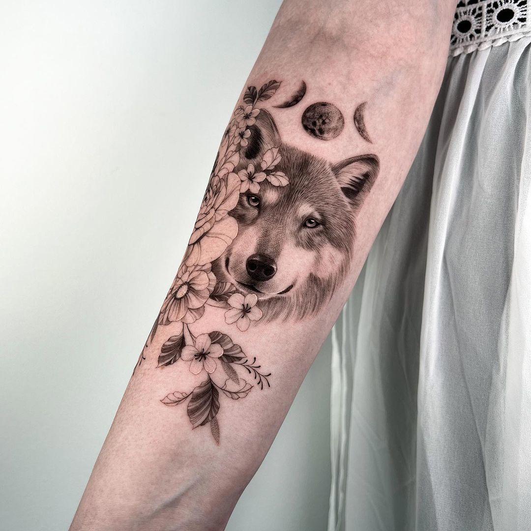 Tatuaje de lobo con flores y lunas en el antebrazo