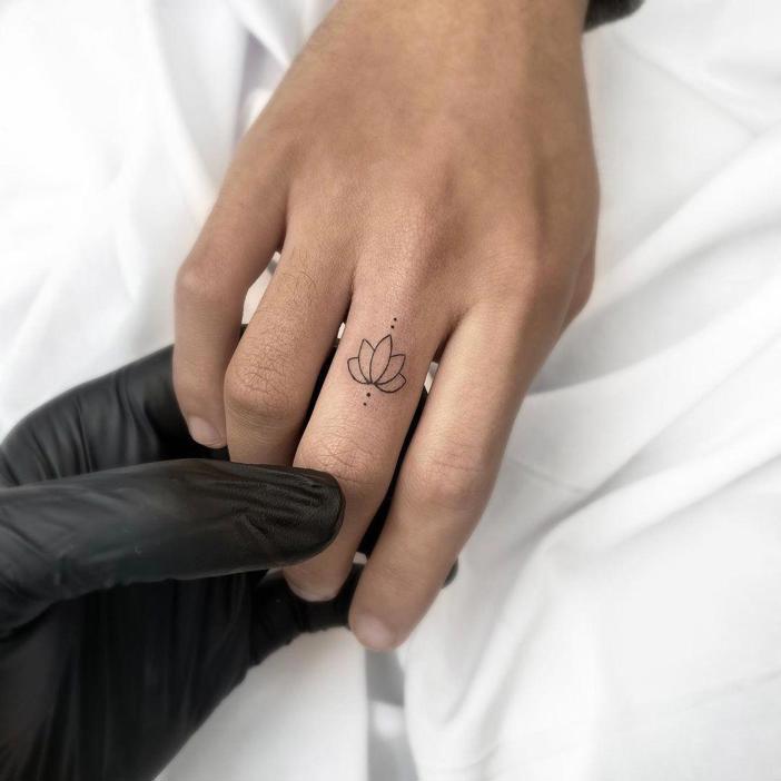 Tatuaje de flor de loto y puntos en el dedo anular
