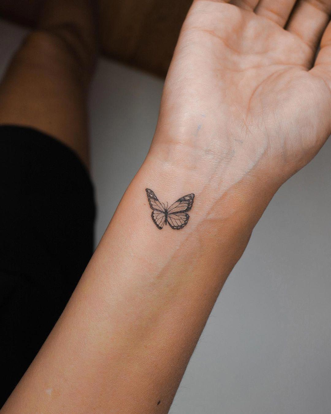 Una pequeña mariposa realista tatuada en la muñec